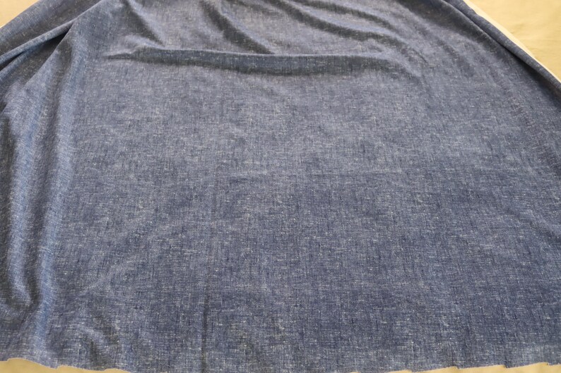 May include: A large expanse of blue fabric with a textured surface. The material is a solid colour with a slightly faded appearance, and it appears to be draped or folded. The fabric has a soft, flowing quality.