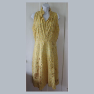 May include: A sleeveless yellow dress with a floral pattern. The dress has a high, ruffled collar and a V-neckline. The fabric is a light, flowing material, and the dress falls to the mid-calf.