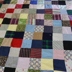 May include: A patchwork quilt composed of various fabric squares in a grid pattern. The squares feature diverse colors and patterns, including stripes, plaid, floral, and solid colors. The quilt is a mix of textures and hues.