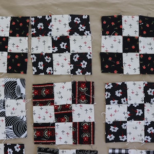 Może przedstawiać: Dziewięć kwadratów z tkaniny, każdy wykonany z czterech mniejszych kwadratów, z różnymi wzorami. Wzory obejmują czarno-białe nadruki kwiatowe, czarno-białe paski i czerwono-czarne paski. Kwadraty są ułożone w trzy rzędy po trzy.