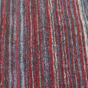 May include: Close-up of a fabric with a vertical striped pattern. The design features a mix of colors, including red, white, purple, and black, creating a textured appearance. The stripes vary in width and intensity.