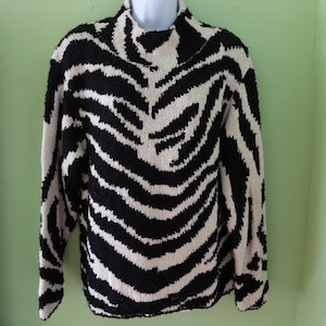 May include: A black and white zebra-striped sweater with a mock turtleneck. The sweater is made of a textured knit fabric and has long sleeves. The zebra pattern is bold and covers the entire sweater.