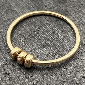 Könnte beinhalten: Ein goldenes Armreif-Armband mit drei runden Perlen. Das Armband ist schlicht und elegant.