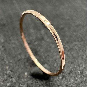 May include: A thin, hammered rose gold band ring with a small, clear gemstone.