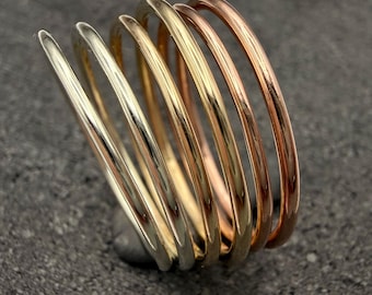 Pode incluir: Um anel de várias bandas com cinco aros de metal finos, lisos e polidos, dispostos num design em espiral ou empilhado. As bandas mudam de cor de um tom prateado para um tom dourado e, finalmente, para um acabamento em ouro rosa quente.