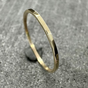 May include: A thin, gold-coloured ring with a faceted, hammered surface texture. The band features a reflective, polished finish that catches the light, creating distinct highlights along its angular, multi-sided outer edge.