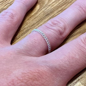 May include: A thin, delicate ring featuring a continuous chain-link design. The ring is crafted from a polished, reflective silver-toned metal, showcasing a series of small, interconnected circular links that form a flexible, lightweight band.