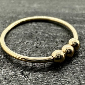 May include: A gold bangle bracelet with three round beads.