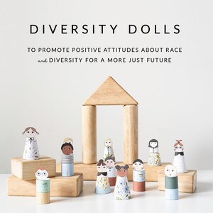 May include: A set of paper dolls representing diversity, standing in front of a wooden block structure. The dolls are all different races and ethnicities, and they are wearing different clothes. The text "DIVERSITY DOLLS" is at the top of the image, and the text "TO PROMOTE POSITIVE ATTITUDES ABOUT RACE and DIVERSITY FOR A MORE JUST FUTURE" is below the dolls.