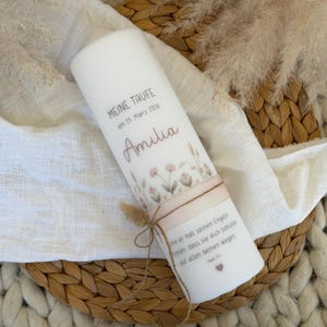 May include: White pillar candle with the text "MEINE TAUFE am 25. März 2026 Amilia" and a floral design. The candle is wrapped with a ribbon and twine, and has a quote printed on it.