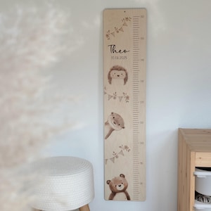 Könnte beinhalten: Holz-Wachstumstabelle mit hellem Holzfinish. Die Tabelle zeigt ein gedrucktes Lineal in Zentimetern sowie Illustrationen eines Igels, eines Otters und eines Bären. Der Name "Theo" und das Datum 10.08.2025 sind auf der Tabelle aufgedruckt.