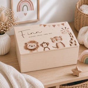 Peut inclure: Une boîte à souvenirs rectangulaire en bois clair avec une illustration imprimée d'un lion, d'un singe, d'un tigre et d'une girafe. Le couvercle porte le nom Finn, la date 20.09.2025, l'heure 11.56 Uhr et les mesures 3.280g et 50cm.