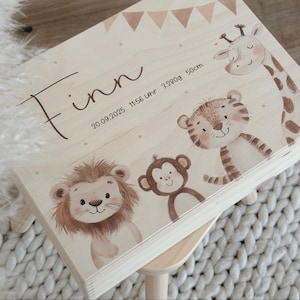 Op de afbeelding: Een lichtgekleurde houten kist met een geschilderd jungle-dieren thema. De kist heeft een giraf, tijger, aap en leeuw. De naam "Finn" staat op de kist, samen met de datum, tijd, gewicht en lengte van een baby.