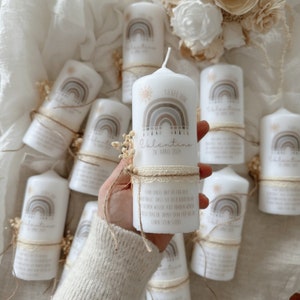 Puede incluir: Un conjunto de velas blancas con un diseño de arcoíris y el texto "TAUFE VON Valentina 24 APRIL 2029". Cada vela está atada con una cinta de encaje blanca y una cuerda marrón.