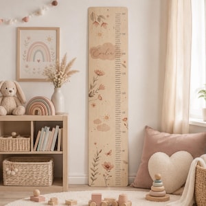 Op de afbeelding: Een hoge, rechthoekige houten groeimeter met een print van bloemen, zonnetjes en wolken in zachte pasteltinten. De naam "Emilia" staat op een wolkje gedrukt. Een verticale schaal meet de lengte van 80 tot 160 centimeter.