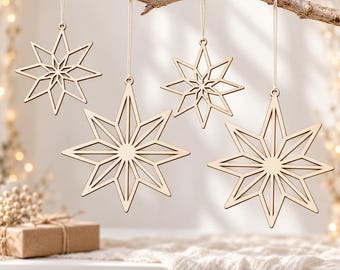 Op de afbeelding: Vier lichtgekleurde houten sterornamenten met ingewikkelde geometrische uitsparingen, hangend aan een tak met dunne touwtjes. De ornamenten variëren in grootte en hebben een veelpuntig sterontwerp met een gladde, natuurlijke houten afwerking.