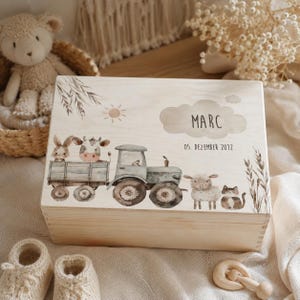 May include: A rectangular wooden keepsake box featuring a printed illustration of a green tractor pulling a trailer with a rabbit and cow, alongside a sheep and cat. The box displays the name MARC and the date 05. DEZEMBER 2012 in black text.