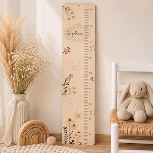 Pode incluir: Uma régua de crescimento vertical em madeira com uma escala impressa de 80 a 160 centímetros. A placa é decorada com ilustrações florais, um sol e uma nuvem contendo o nome Sophie. Inclui um pequeno orifício no topo para pendurar.