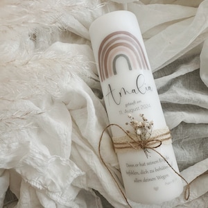 May include: White baptism candle with a rainbow design and the name "Amalia" written in cursive. The candle also includes the date "11. August 2024" and a quote in German.