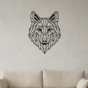 Op de afbeelding: Een geometrisch wolfskop wanddecor van zwart metaal, hangend aan een witte muur boven een beige bank en een houten salontafel.
