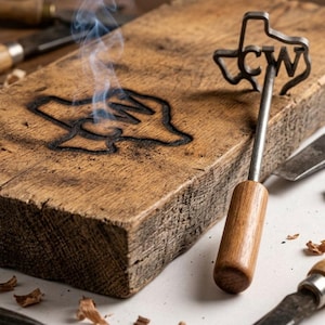 May include: A branding iron with a Texas-shaped head and the letters "CW" is shown next to a wooden block with a branded image. Smoke rises from the branded image on the wood. The branding iron has a wooden handle and a metal shaft.