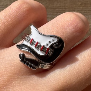 May include: A silver ring shaped like a black and white electric guitar with red accents.