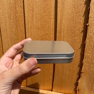 Puede incluir: Una peque&ntilde;a caja met&aacute;lica rectangular de color plateado con esquinas redondeadas y una tapa plana y lisa. El recipiente presenta un dise&ntilde;o sencillo y funcional con una construcci&oacute;n sin costuras, mostrando un acabado met&aacute;lico limpio y uniforme.