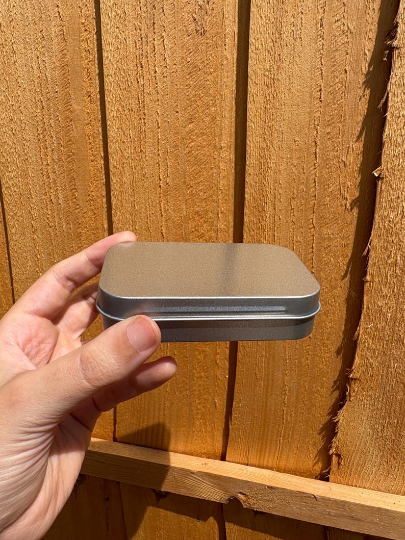 Puede incluir: Una peque&ntilde;a caja met&aacute;lica rectangular de color plateado con esquinas redondeadas y una tapa plana y lisa. El recipiente presenta un dise&ntilde;o sencillo y funcional con una construcci&oacute;n sin costuras, mostrando un acabado met&aacute;lico limpio y uniforme.