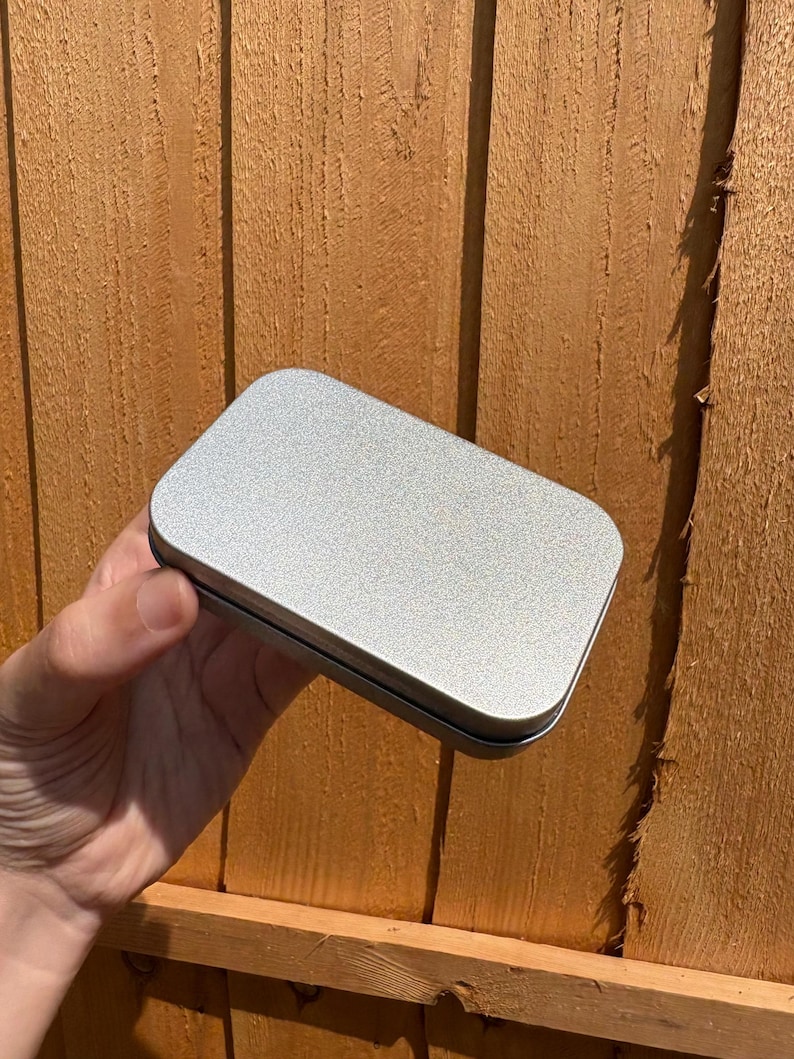 Puede incluir: Una caja met&aacute;lica rectangular de color plateado con esquinas redondeadas y un acabado mate liso. El recipiente cuenta con una tapa plana sencilla que encaja firmemente sobre la base, presentando una superficie met&aacute;lica limpia y uniforme.