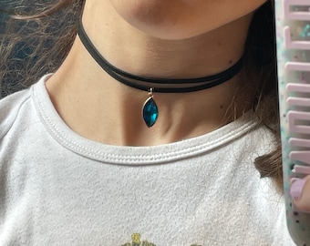 Op de afbeelding: Een zwarte choker ketting met een traanvormige blauwe edelsteen hanger.