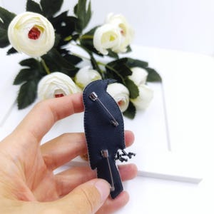 May include: Black embroidered bird brooch with black beads and a silver pin on the back.
