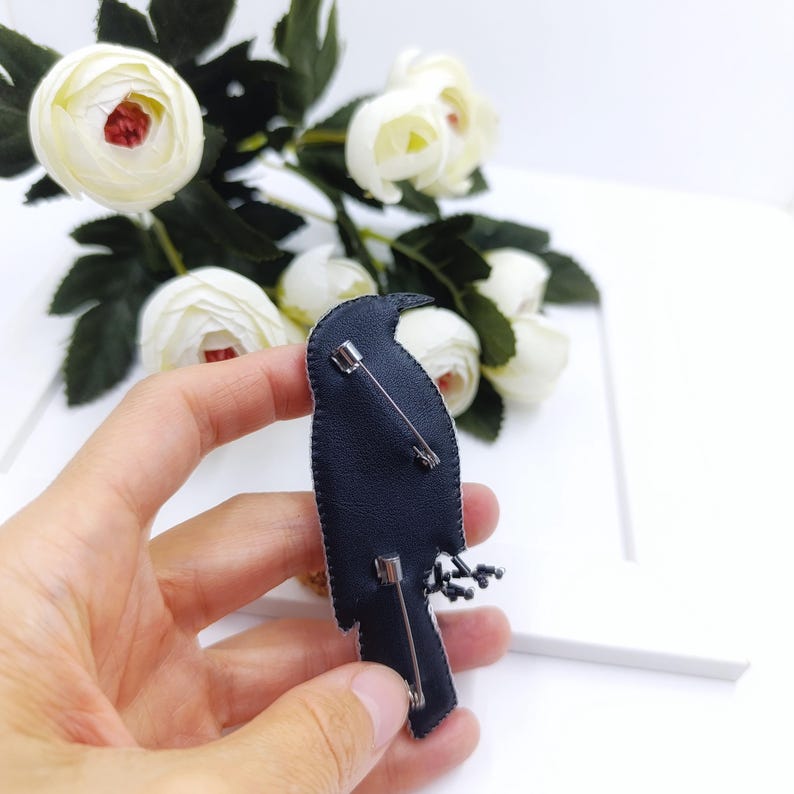 May include: Black embroidered bird brooch with black beads and a silver pin on the back.