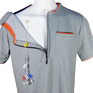 May include: Gray short-sleeved shirt with a zipper down the front and orange trim. The shirt has a pocket on the right side with orange trim. A medical IV line is visible through the open front of the shirt.
