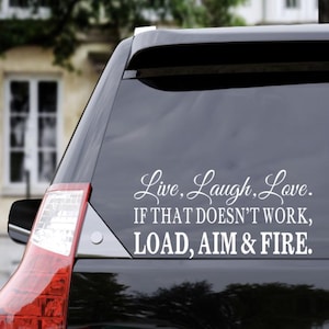 May include: Black vehicle rear window decal with the text "Live, Laugh, Love. If that doesn't work, LOAD, AIM & FIRE." The decal is in white script and sans-serif fonts. The vehicle's taillight is visible.