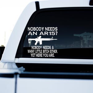 May include: White vinyl decal applied to a vehicle's rear window. The decal features the silhouette of an AR-15 rifle and the text: "NOBODY NEEDS AN AR15? NOBODY NEEDS A WHINY LITTLE BITCH EITHER, YET HERE YOU ARE."