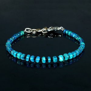 Op de afbeelding: Een blauwe opaal en zwarte kralen armband met een zilveren sluiting. De armband is gemaakt van kleine, ronde kralen en heeft een delicate, elegante uitstraling.