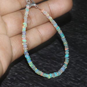 Peut inclure: Un bracelet délicat composé de perles d'opale irisées. Les perles sont petites et rondes, et elles sont enfilées sur une chaîne en argent. Le bracelet est un bijou magnifique et unique.