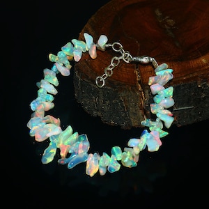 Peut inclure: Un bracelet en chaîne argent avec une fermeture à fermoir. Le bracelet est composé de plaquettes d'opale blanche irisée.