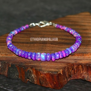 May include: A purple and pink Ethiopian opal beaded bracelet with a silver clasp. The bracelet is on a wooden surface.