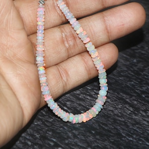May include: A white opal gemstone necklace with a silver clasp. The necklace is made of small, round beads that are strung together on a thin chain.