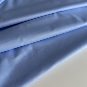 May include: A light blue fabric with a smooth texture. The fabric is folded in a way that shows the texture and color.
