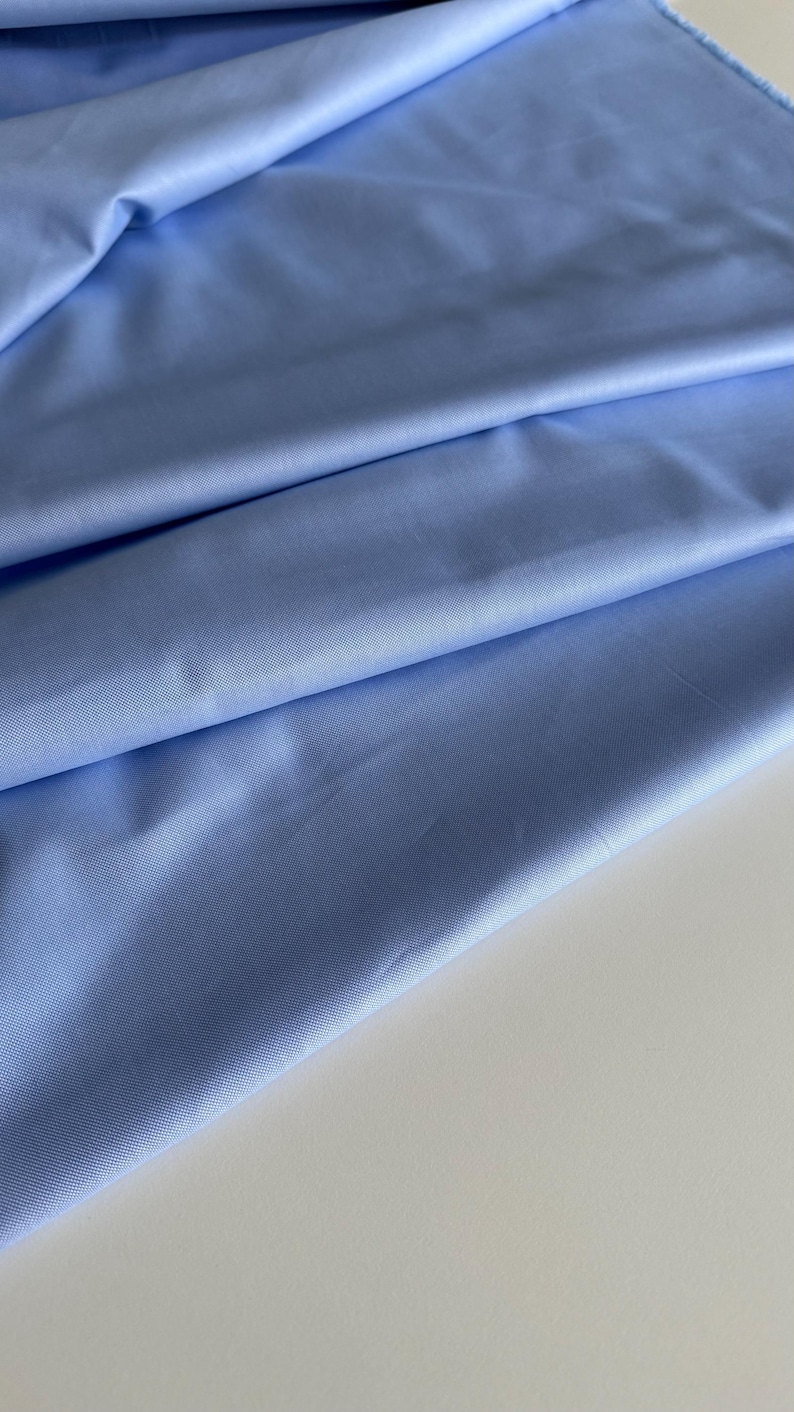 May include: A light blue fabric with a smooth texture. The fabric is folded in a way that shows the texture and color.