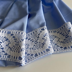 May include: A light blue fabric with a white lace trim. The fabric is folded and the lace trim is visible on the edge.