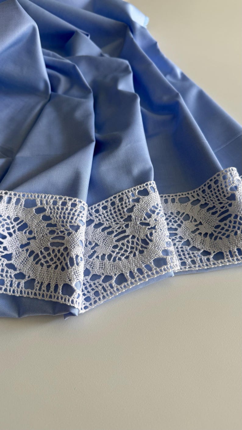 May include: A light blue fabric with a white lace trim. The fabric is folded and the lace trim is visible on the edge.