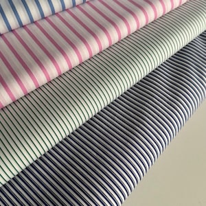 May include: A stack of five different striped fabrics. The top fabric is light blue, the second is white and light blue, the third is pink and white, the fourth is green and white, and the bottom fabric is navy blue and white.