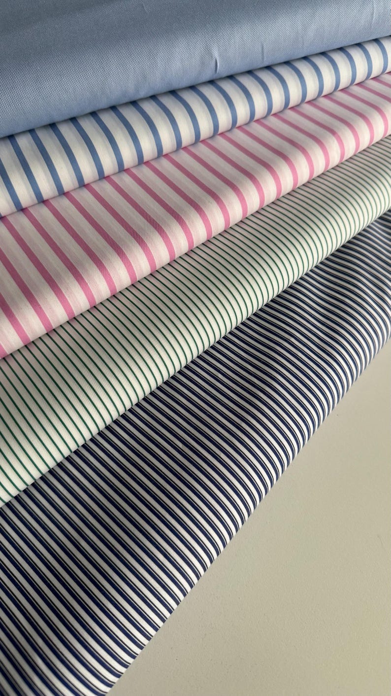 May include: A stack of five different striped fabrics. The top fabric is light blue, the second is white and light blue, the third is pink and white, the fourth is green and white, and the bottom fabric is navy blue and white.
