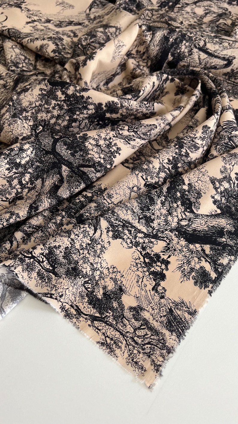 May include: Beige fabric with a black and white toile pattern of trees and branches. The fabric has a raw edge.