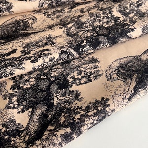 May include: Beige fabric with a black and white repeating pattern of trees and foliage. The fabric is folded over itself, showing the pattern on both sides.