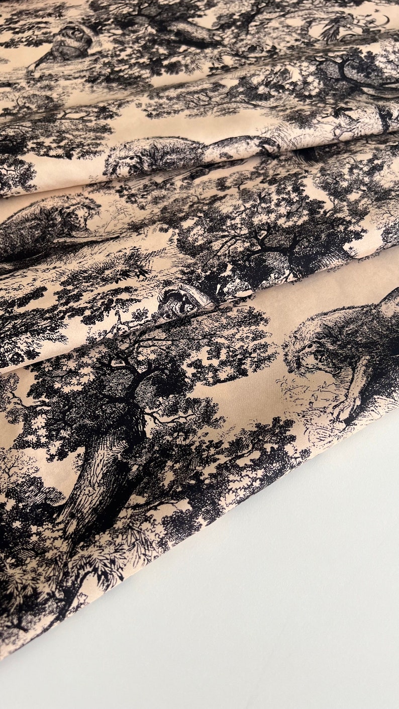 May include: Beige fabric with a black and white repeating pattern of trees and foliage. The fabric is folded over itself, showing the pattern on both sides.
