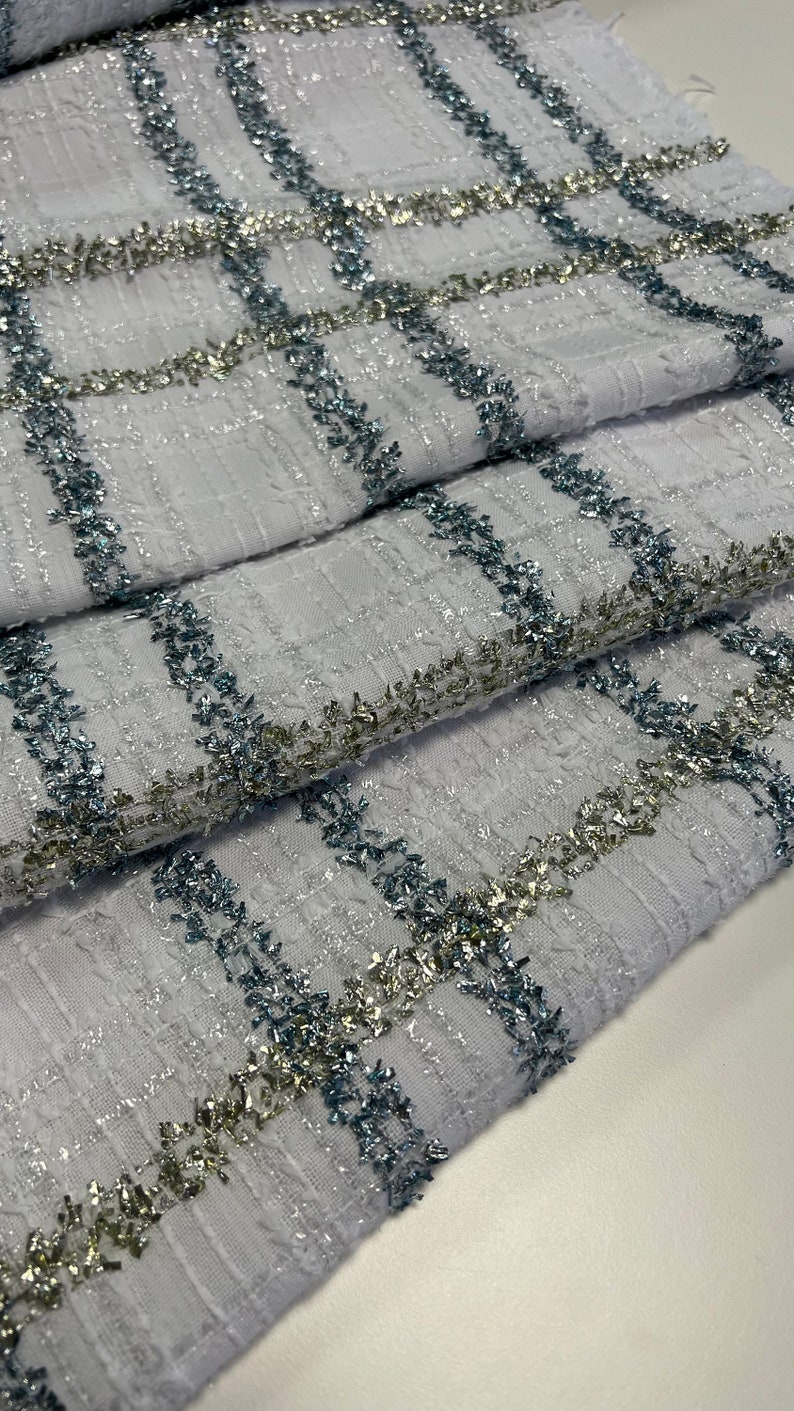 May include: White fabric with a checkered pattern. The fabric is decorated with silver and blue glitter thread.